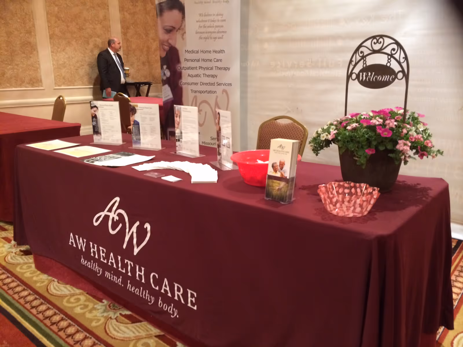 Indoor AW Health Care booth with maroon table, brochures, and welcome sign.