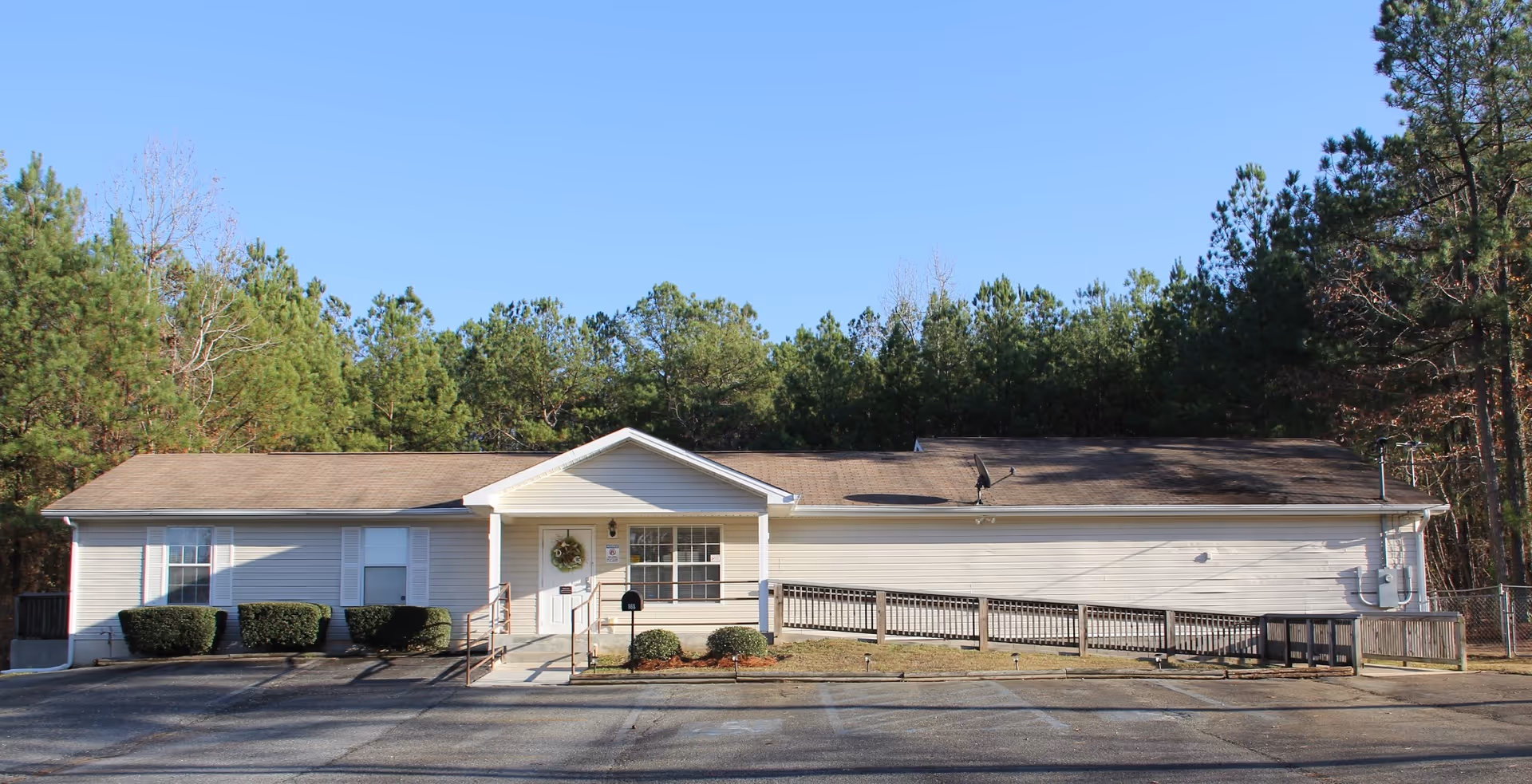 Single-story white facility with front entrance, shrubs, and surrounding trees.