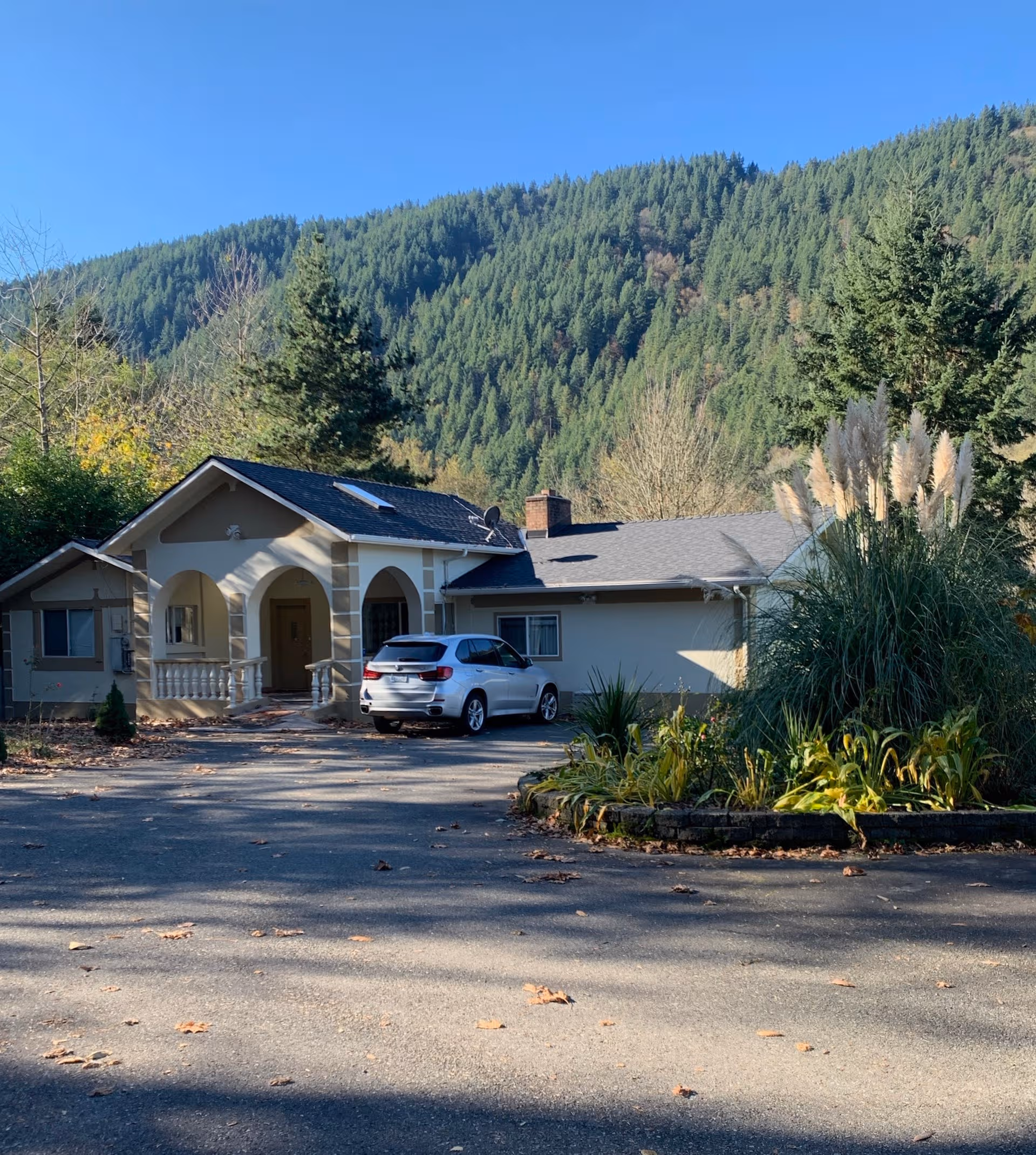 Single-story facility with arched entryways, a driveway, and forested hills behind.