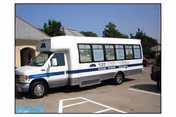 White shuttle bus with blue stripe parked in a lot outside a senior living facility.