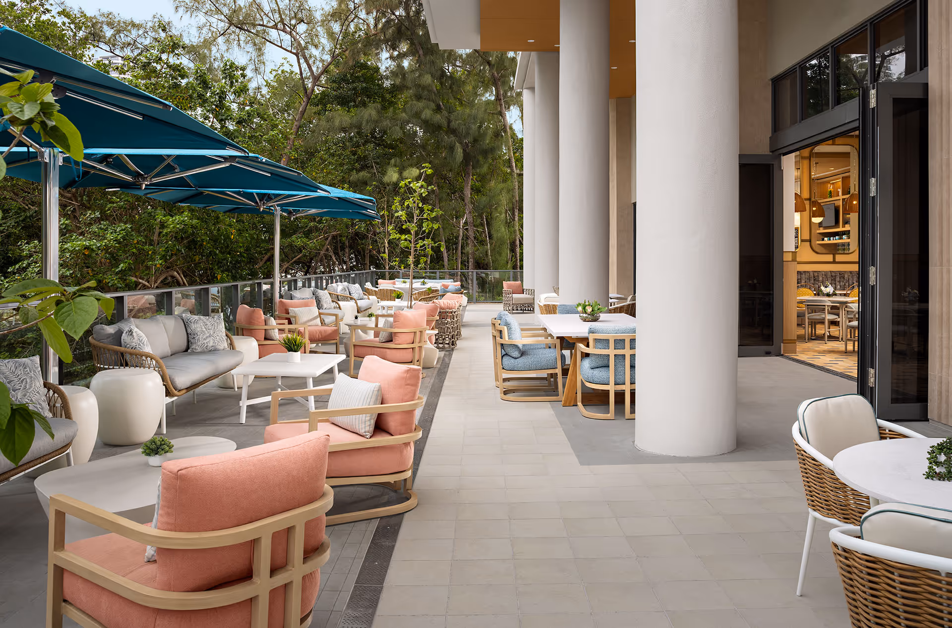 Outdoor patio seating with colorful chairs, tables, and blue umbrellas along a building.