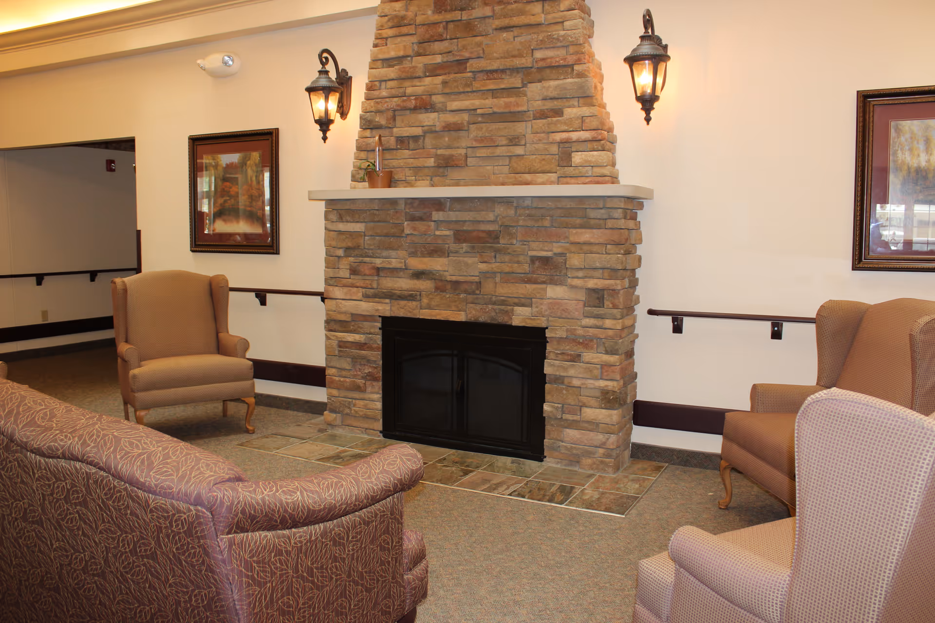 Cozy lounge with stone fireplace, framed art, and cushioned seating in a senior living facility.
