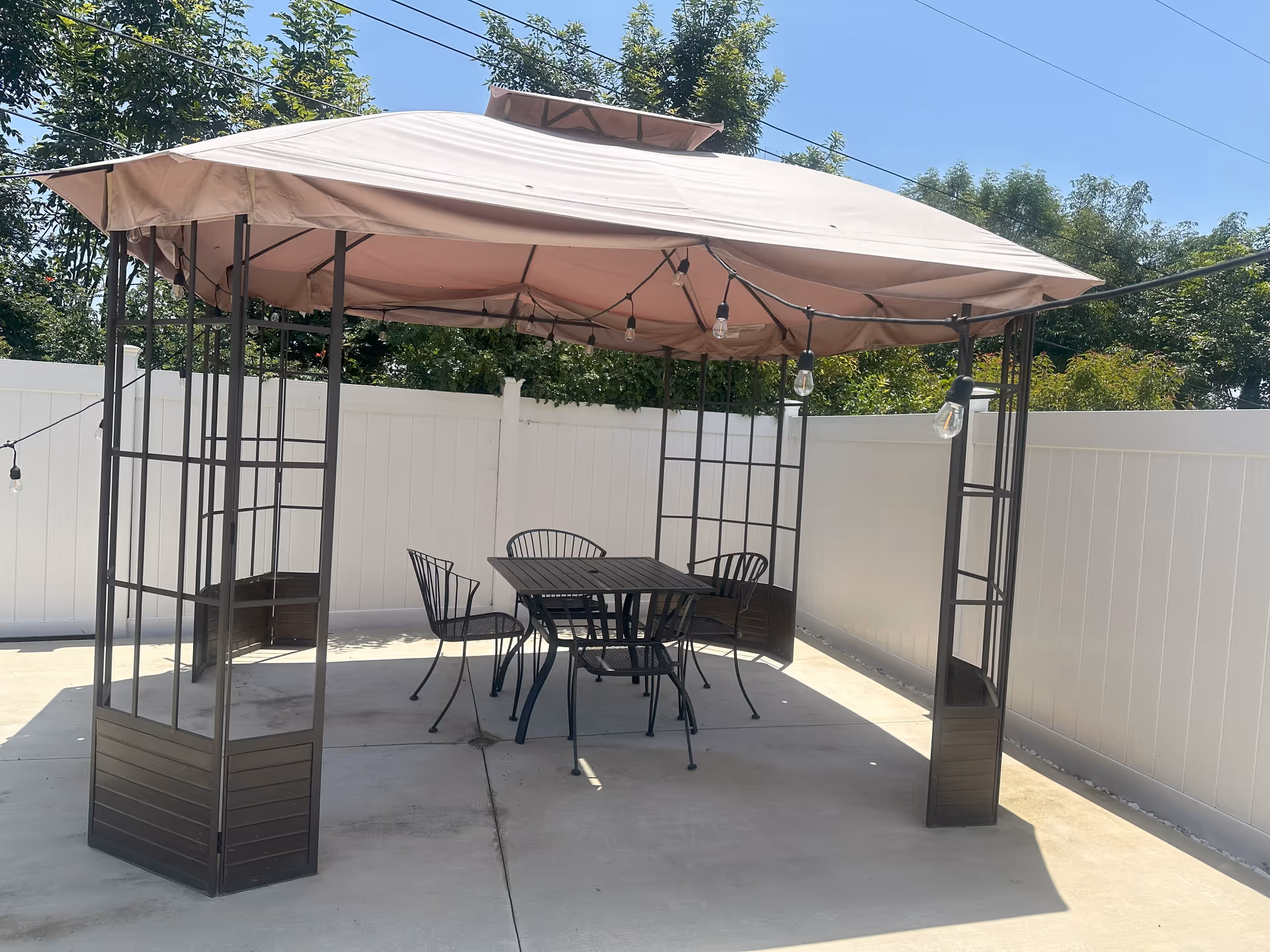 Outdoor patio with a pink canopy, string lights, and metal table and chairs.