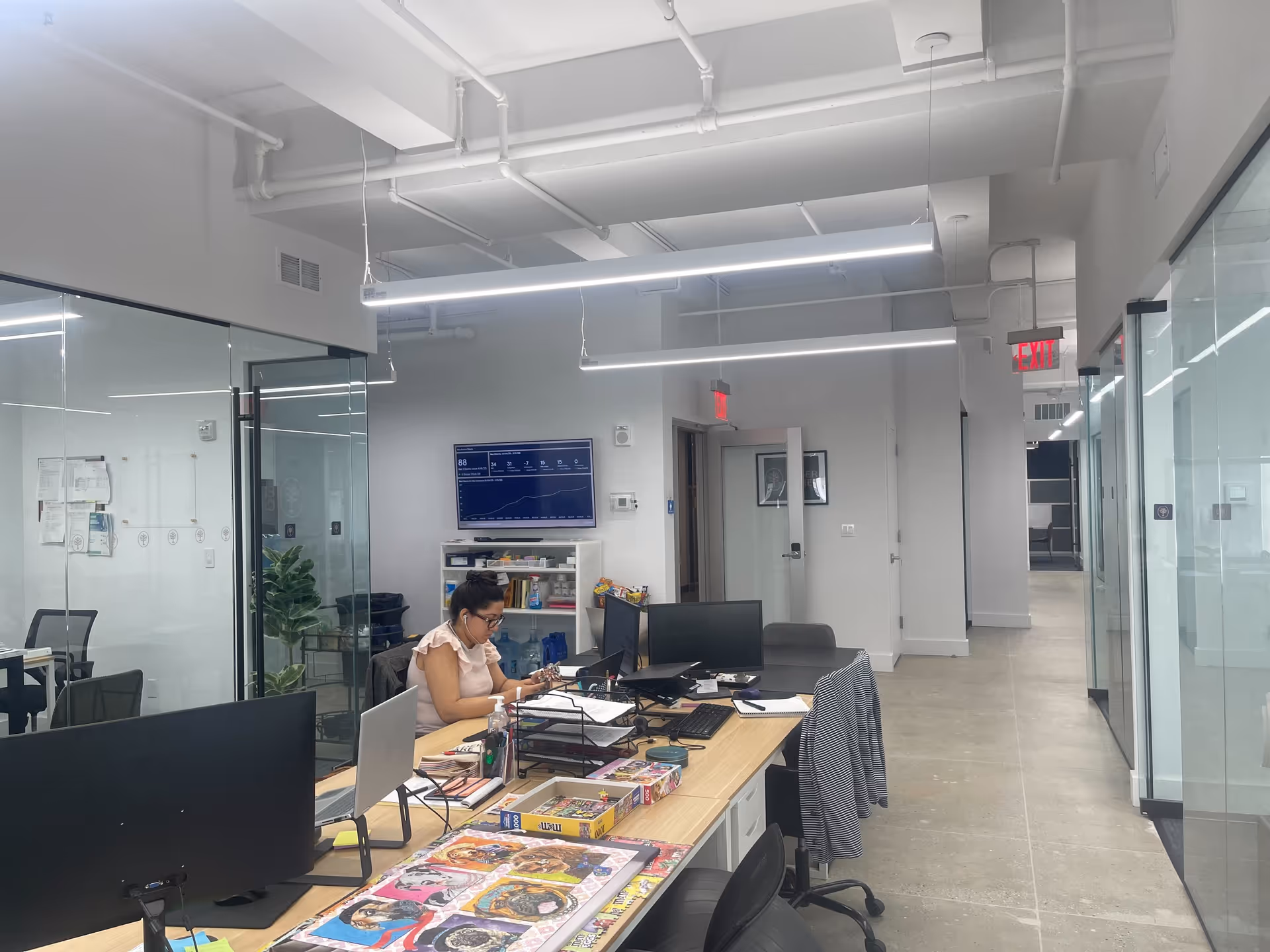 A staff member works at a cluttered desk in a modern glass-walled office.