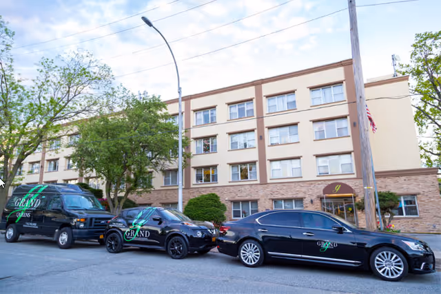 Multi-story beige Grand Rehabilitation and Nursing exterior in Queens with several black cars parked out front.