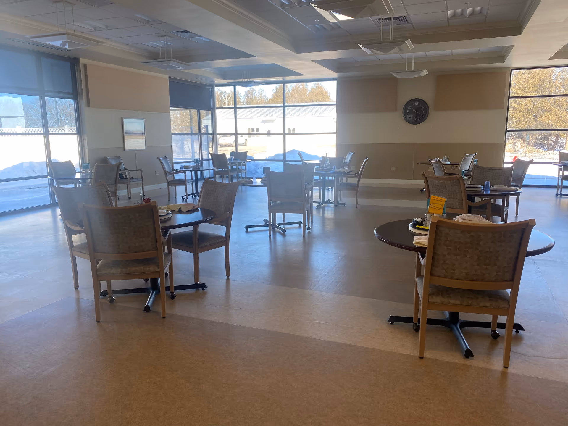 Bright senior living dining room with round tables, chairs, and large windows.