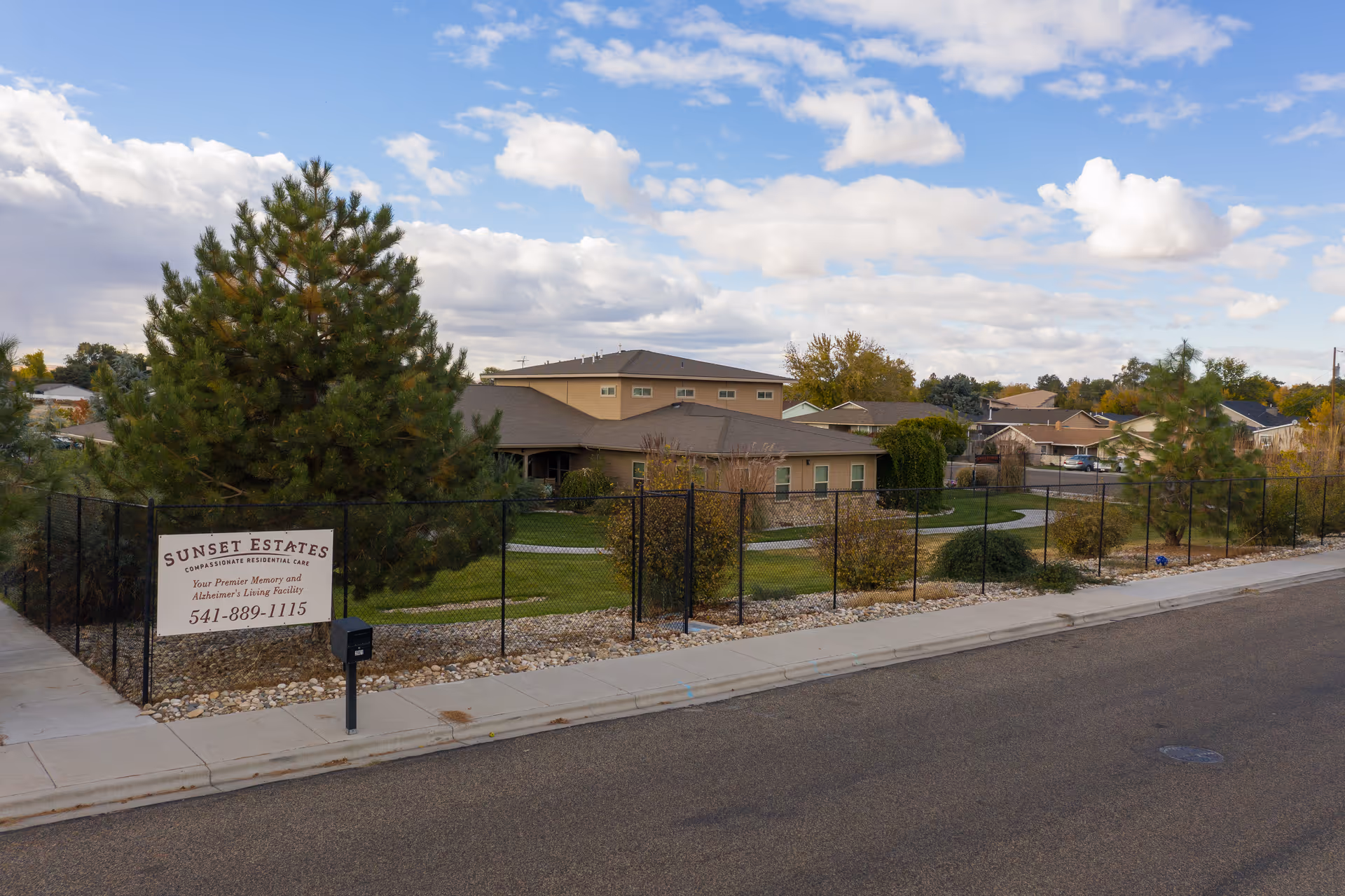 Exterior view of Sunset Estates and Villa with a fenced front yard and sign.