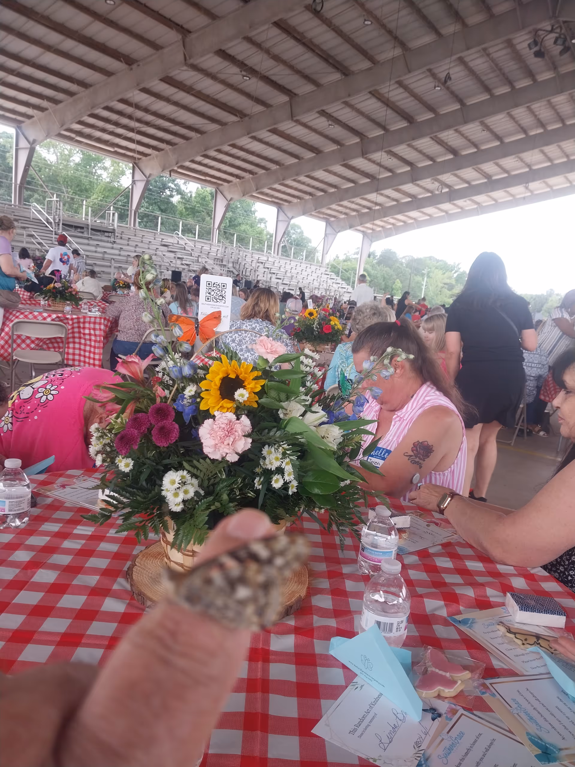 Outdoor pavilion event with checkered tables, flower arrangements, and guests dining.