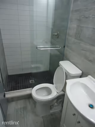 Compact bathroom featuring a toilet, sink, and glass-enclosed shower.