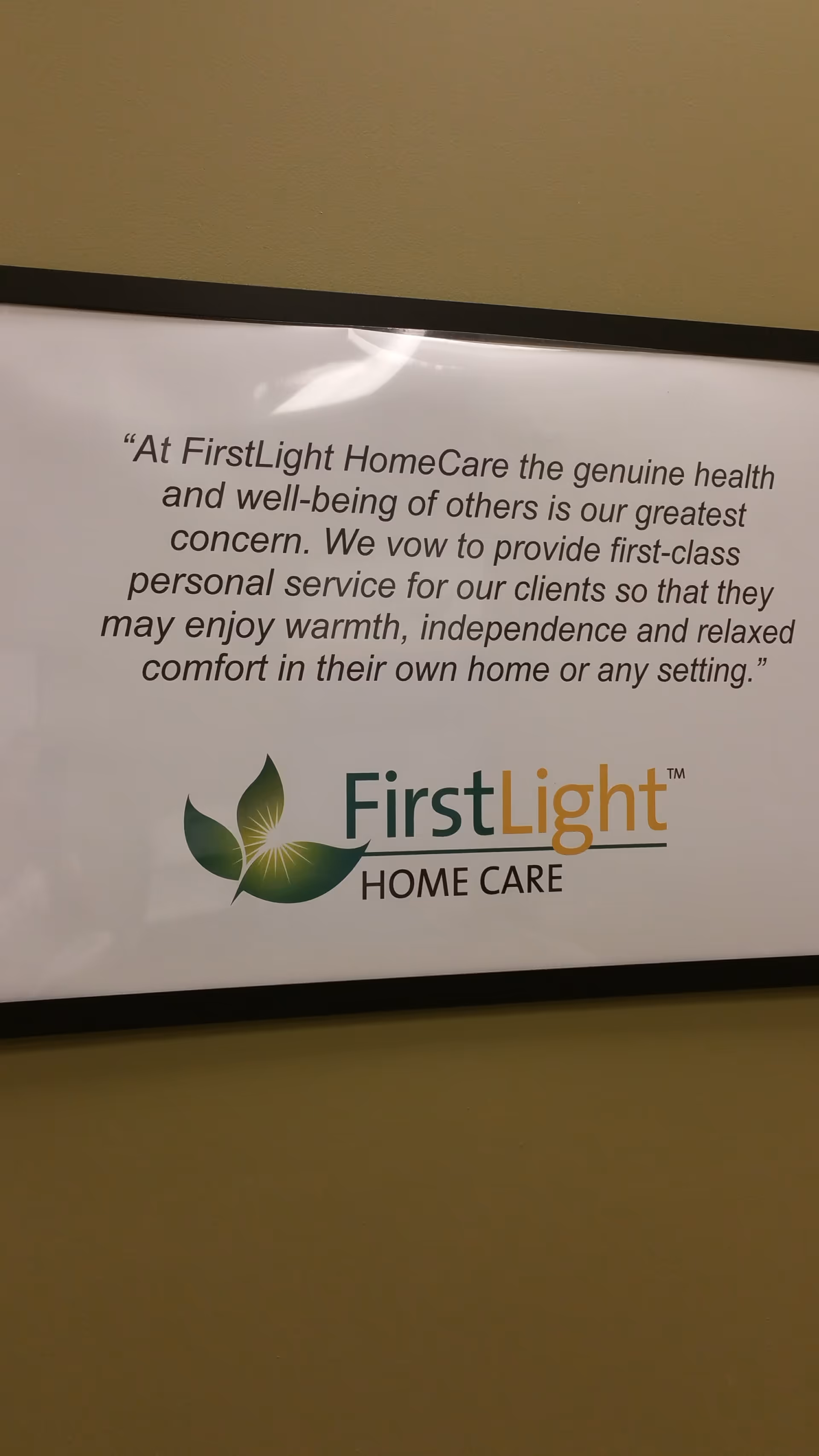 Framed wall sign reading FirstLight Home Care with slogan and green leaf logo.