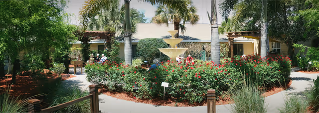 A landscaped outdoor courtyard with a central fountain, palm trees, and flowering shrubs.
