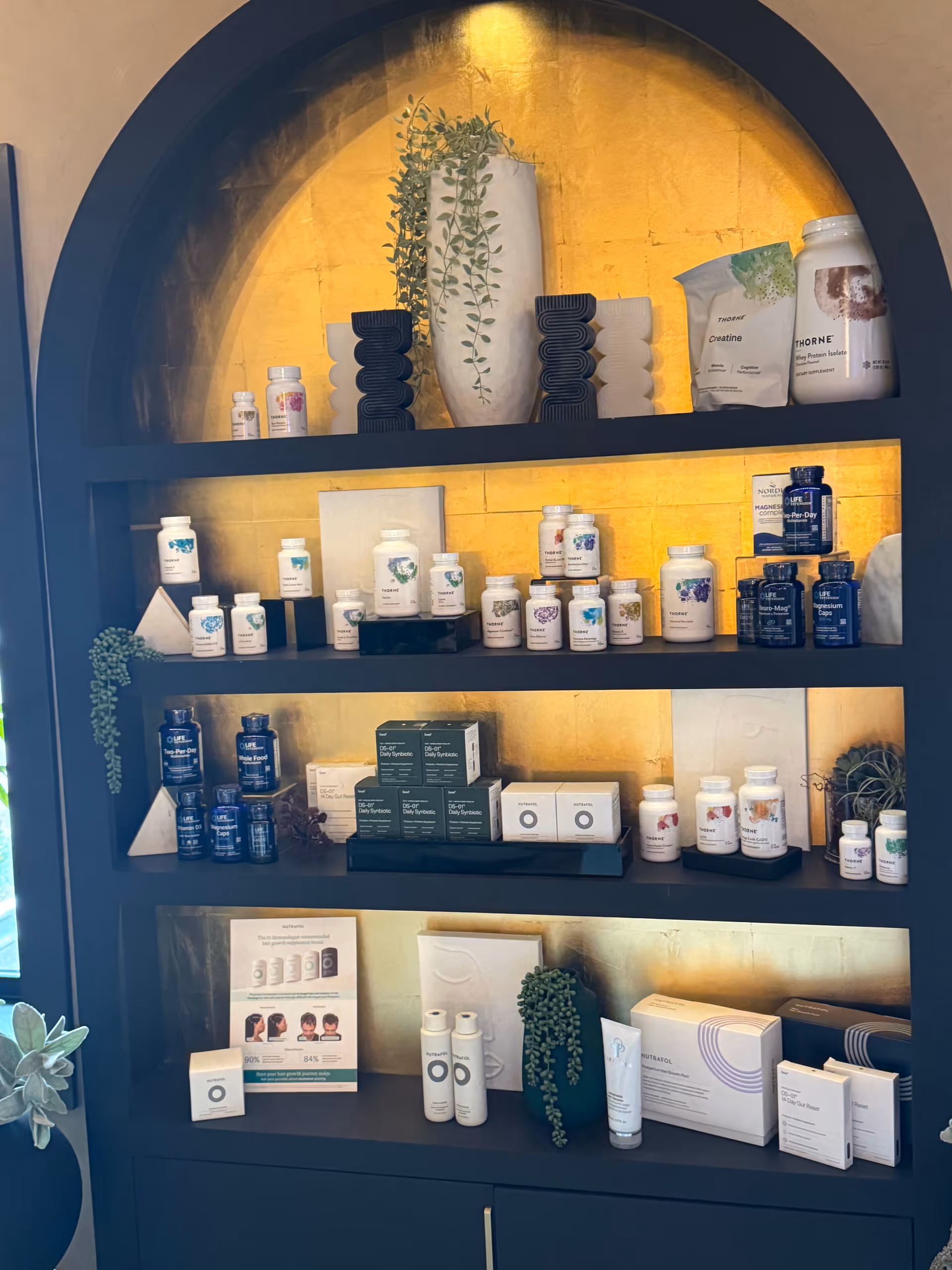 Blue arched shelf displaying vitamins, supplements, and plants against a warm gold backdrop.