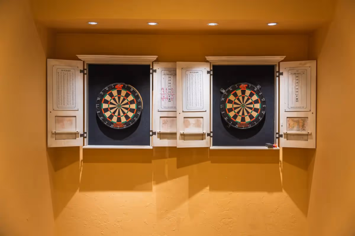 Two dartboards mounted inside white wall cabinets on a yellow interior wall.