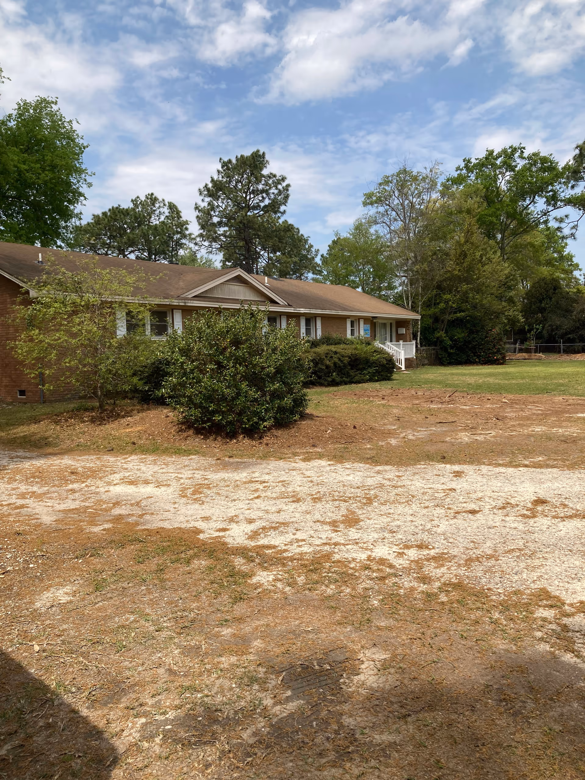 Single-story brick building with a front porch, trees, and a gravel yard.