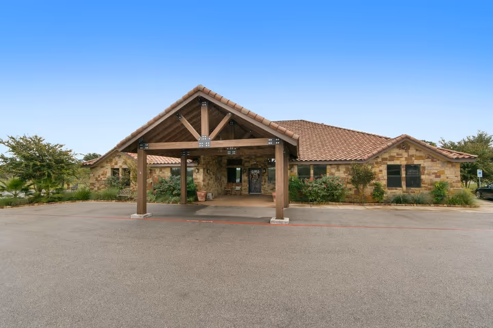 Stone-clad building front with a covered wooden porte-cochere and tiled roof at the facility entrance.
