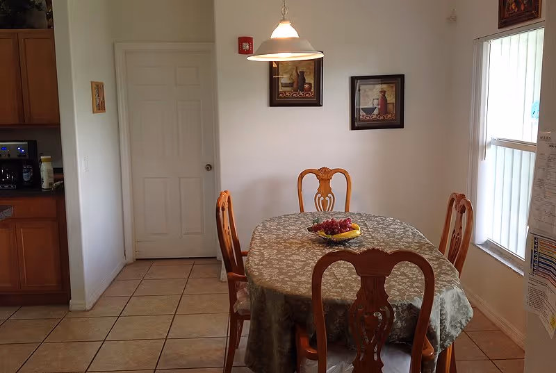A dining room with a round table, chairs, fruit bowl, and pendant light.