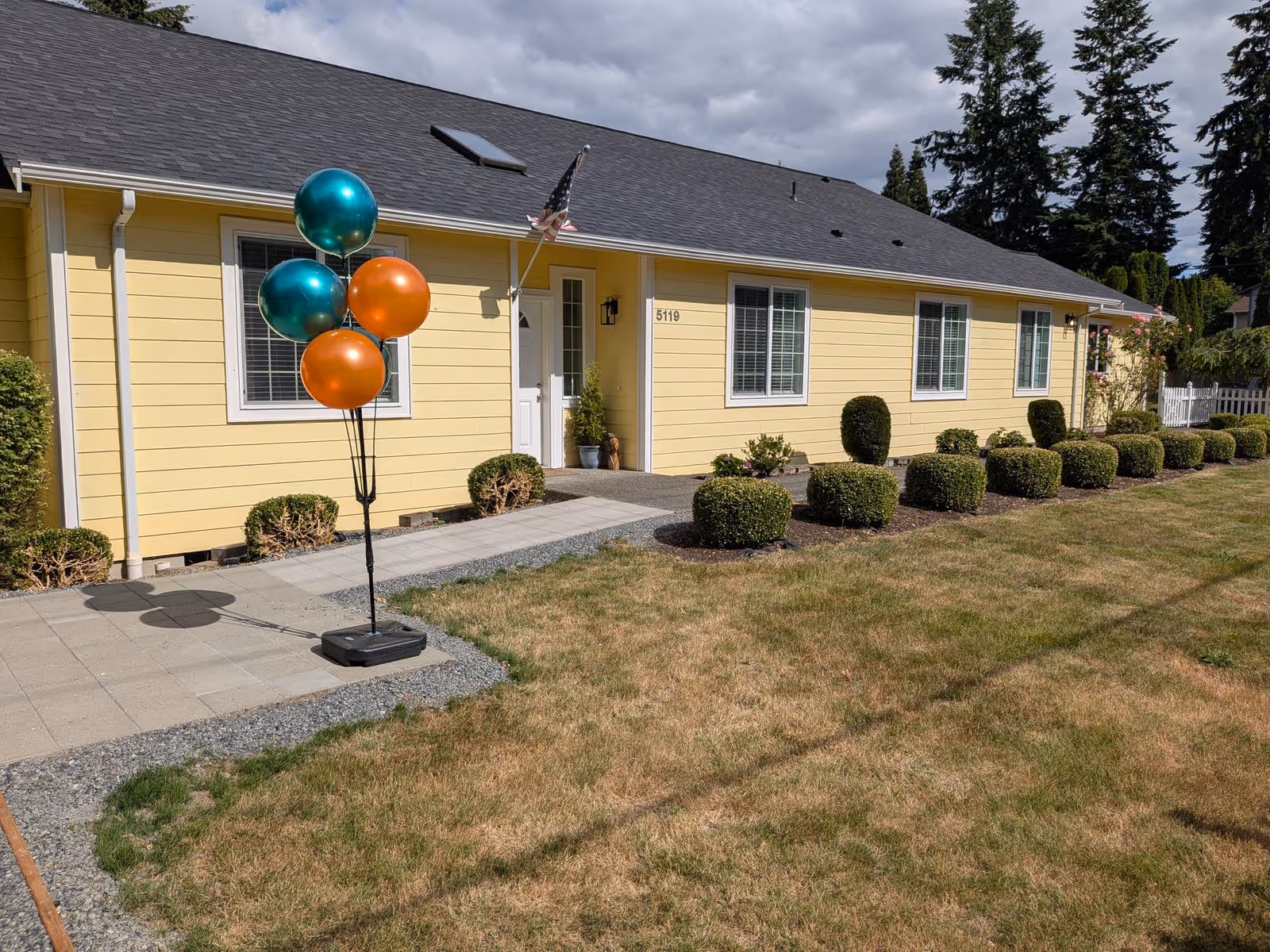 Exterior view of a yellow single-story senior home with balloons at the entrance.