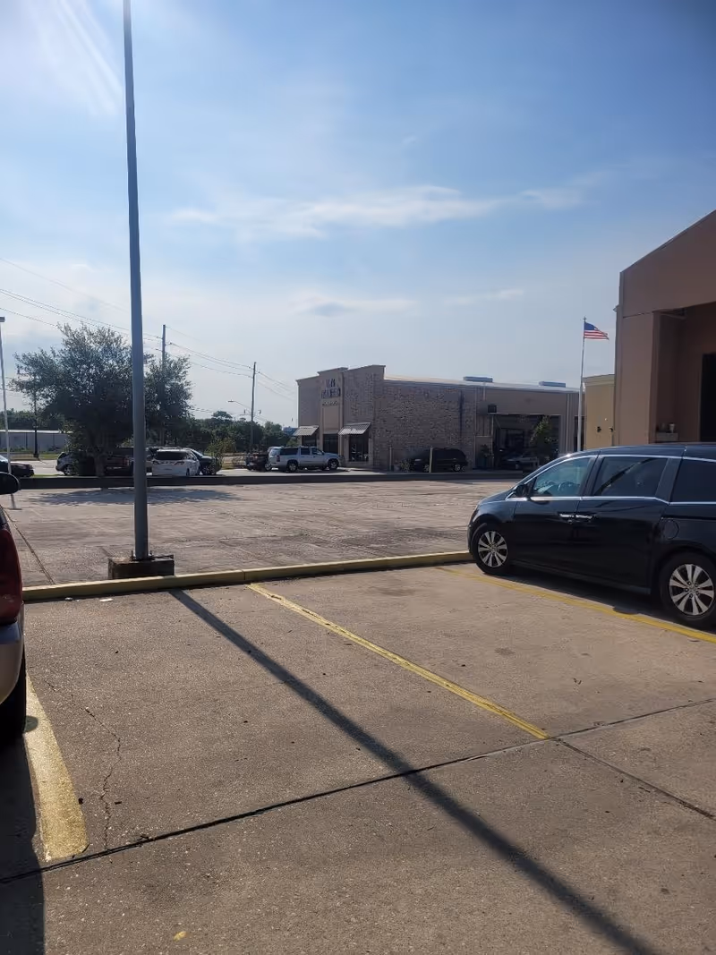 Parking lot in front of a senior care facility with cars, flag, and a beige building.