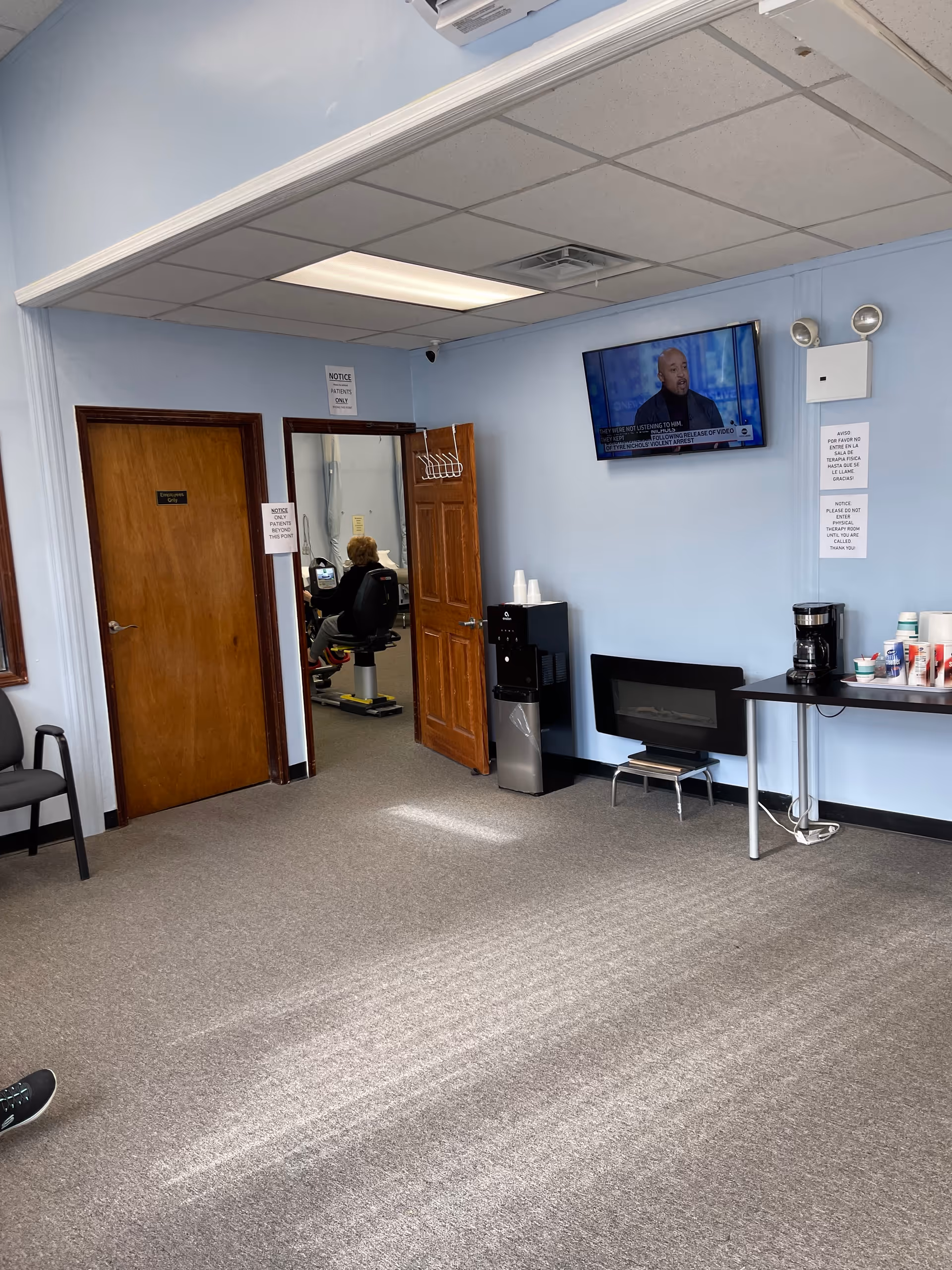 Interior lounge in Fidelity Home Care with coffee station, wall-mounted TV, and doorway.