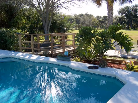 Outdoor pool area with clear blue water, railing, and surrounding greenery.
