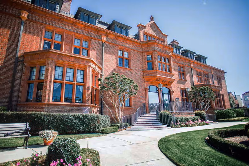 Brick senior living building with arched entrance, stairs, and landscaped grounds.