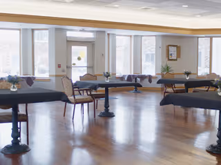Empty dining room with round tables, chairs, and centerpieces in a bright, wooden-floored space.