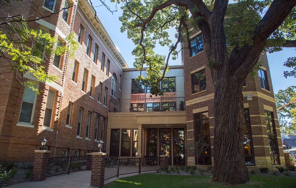 Brick senior living building exterior with a large tree near the entrance.