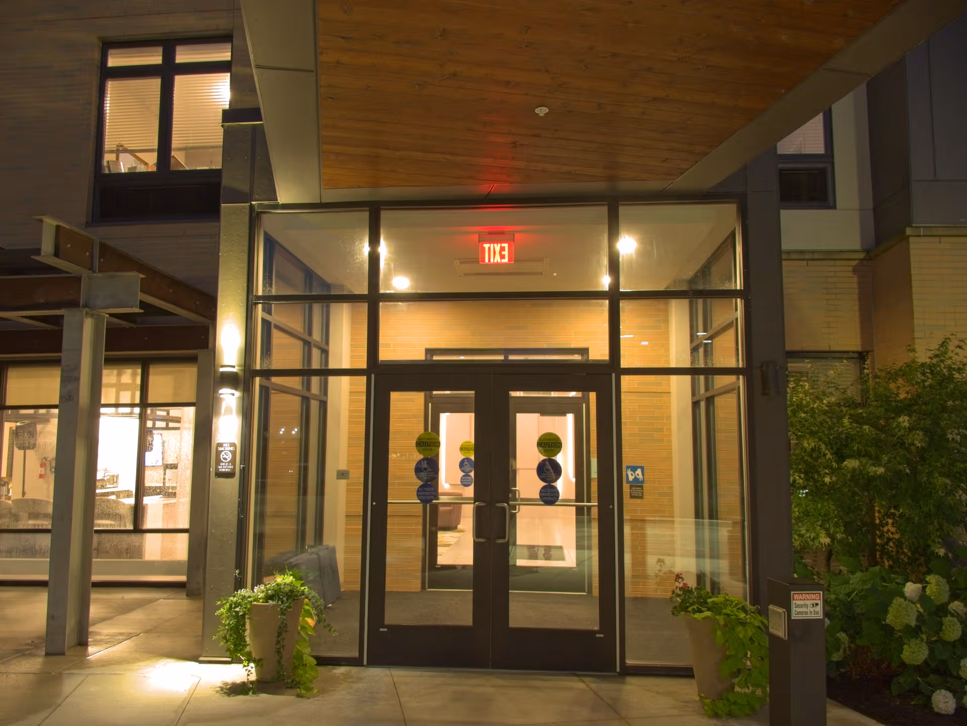 Nighttime view of Ridgecrest of McCandless entrance with glass doors and potted plants.