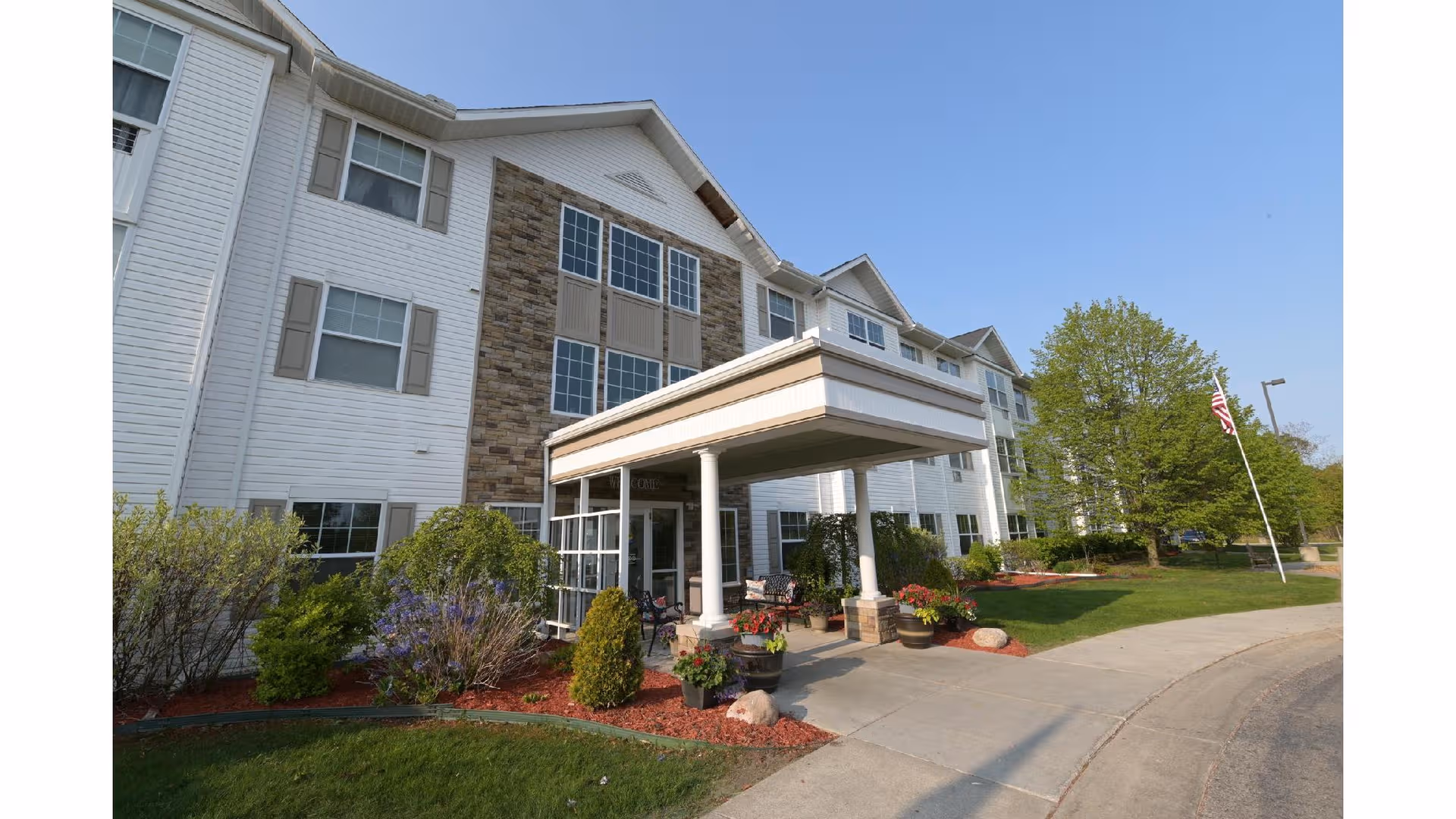 Exterior view of Mercy Village building with entrance canopy, landscaping, and American flag.