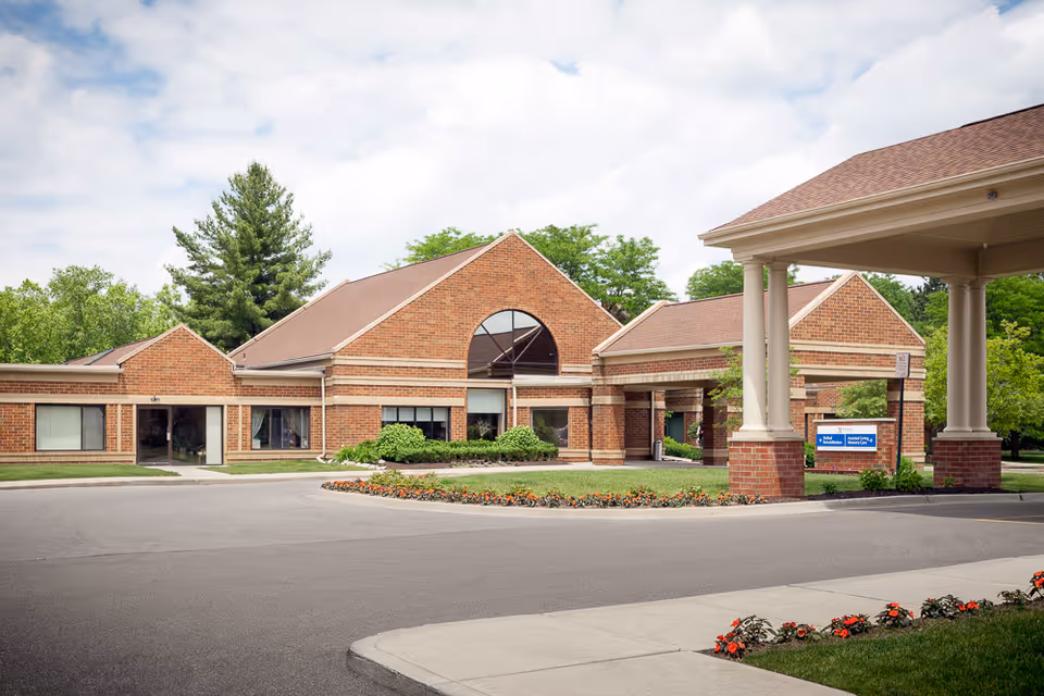Front view of a red brick senior living facility entrance with porte-cochère.