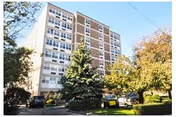 Tall mid-rise senior residence building with parked cars and autumn-colored trees in front.