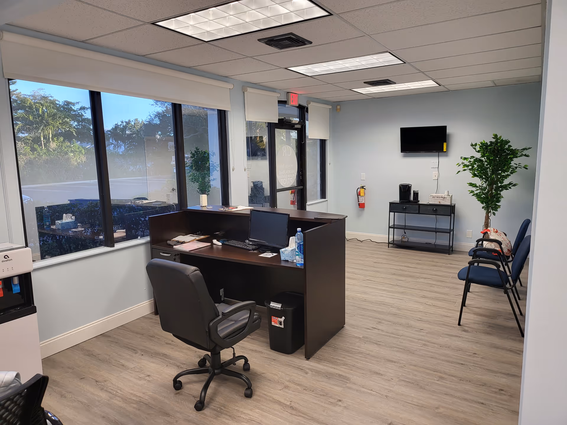 Reception desk with computer, chairs, and a plant in a bright office space.