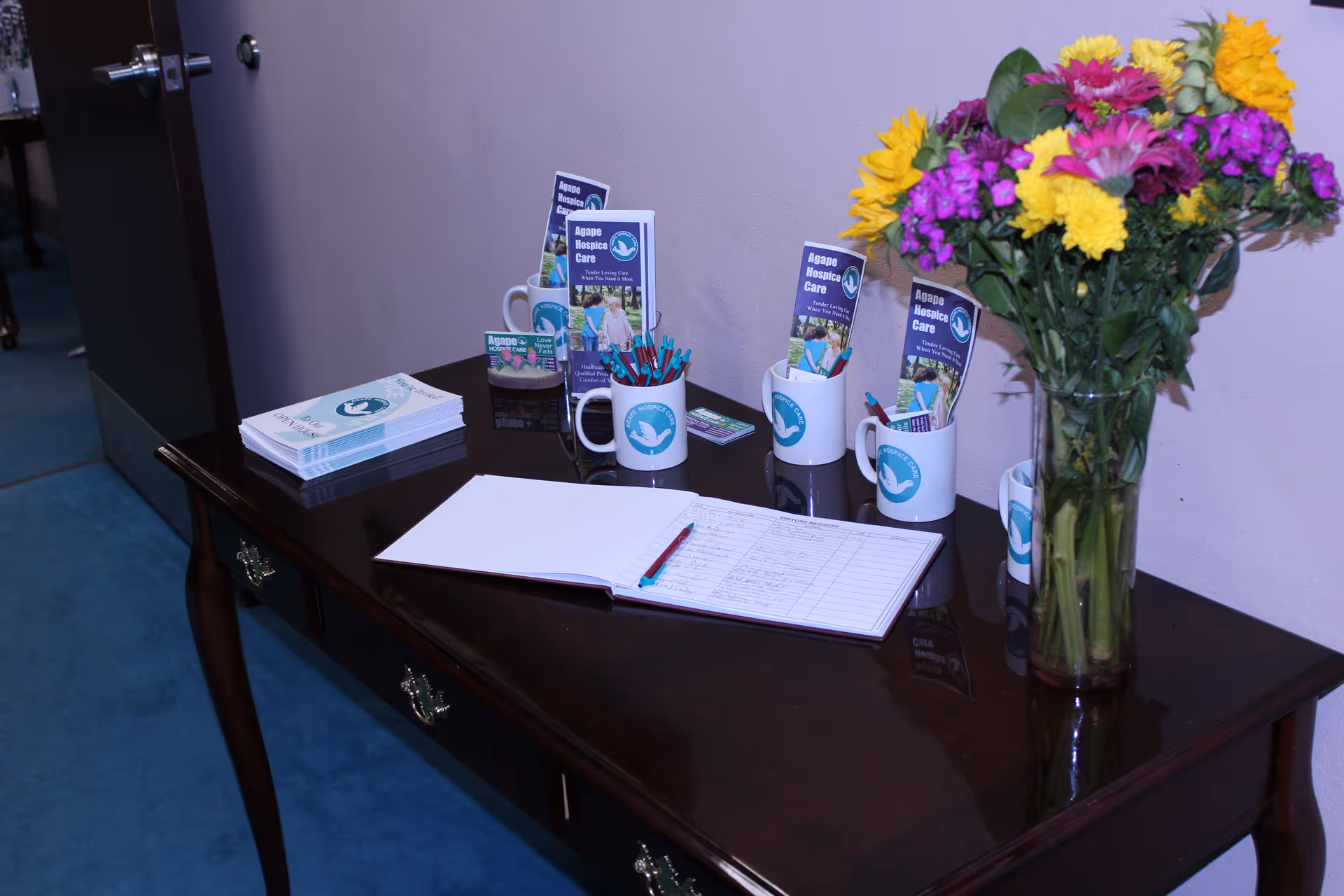 A dark wooden reception desk with brochures, a notebook, pens, and a vase of colorful flowers.