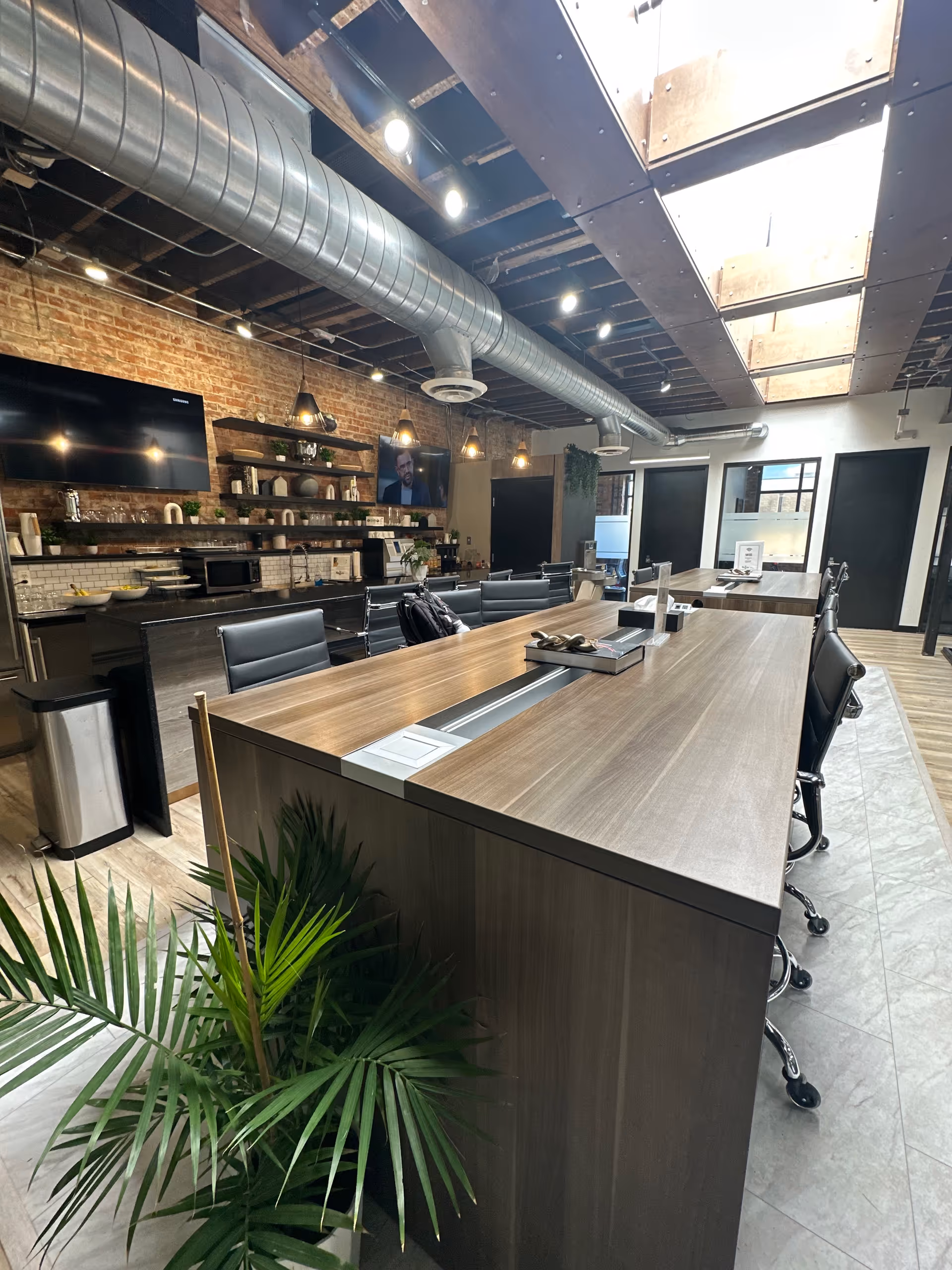 Modern communal dining area with a long wooden counter, pendant lights, and exposed brick wall.