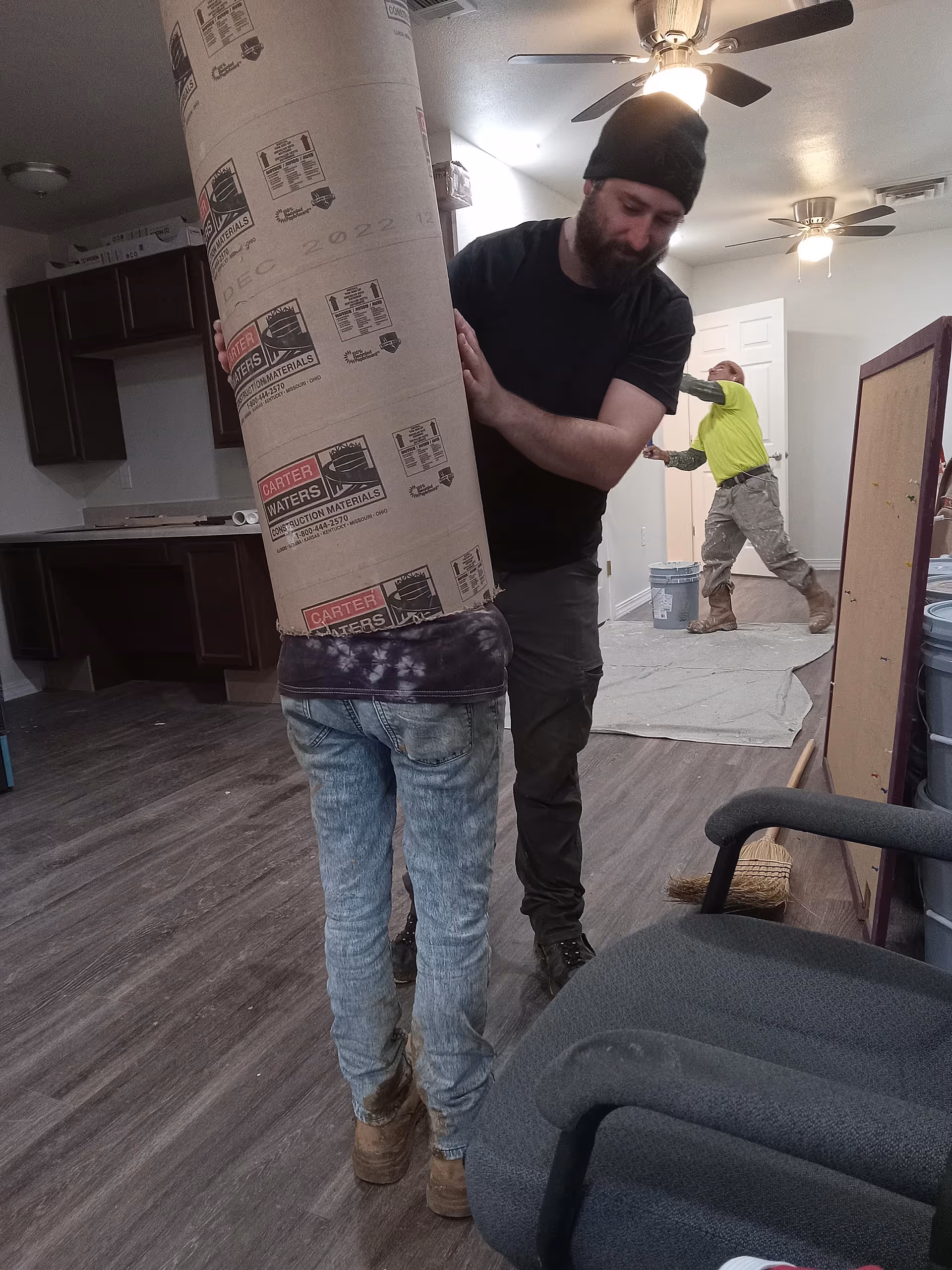 Two workers move a large wrapped item inside a senior living facility interior.