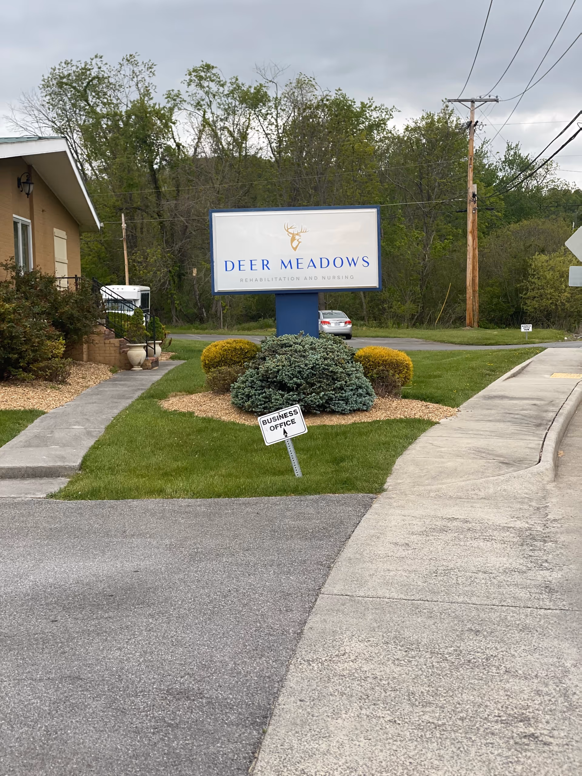 Outdoor scene with a Deer Meadows sign, landscaping, and a building facade on the left
