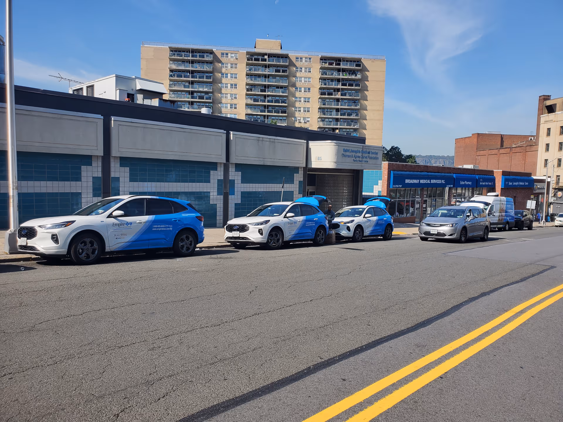 Line of blue-and-white vehicles parked along a street in front of Saint Joseph's Family Health Center