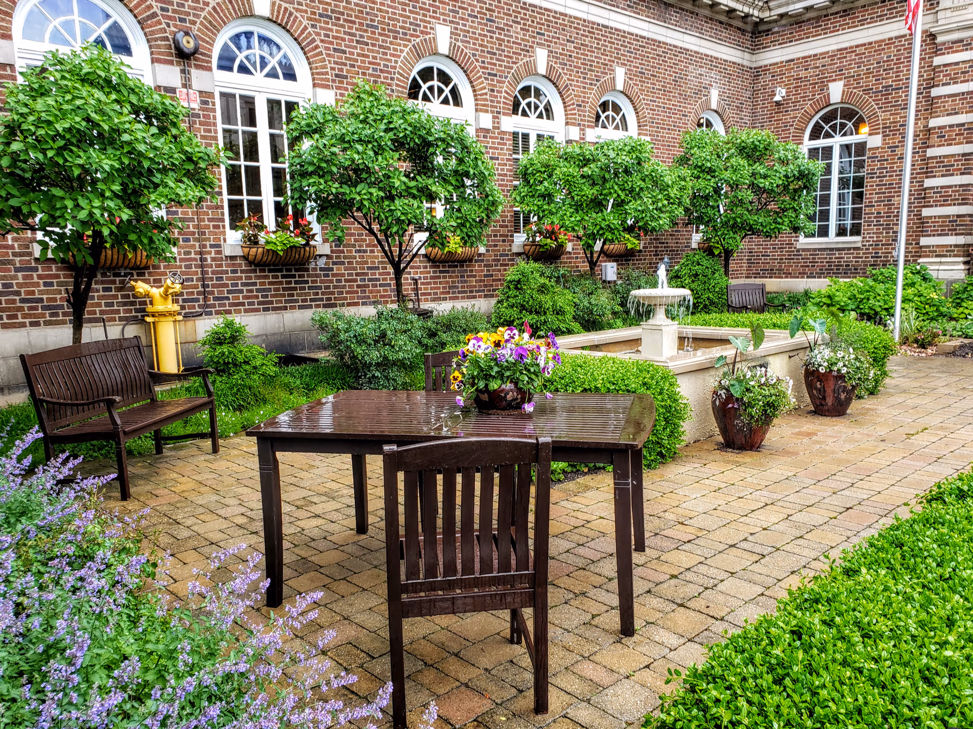 Brick courtyard of a senior facility with patio furniture, greenery, and a central fountain.