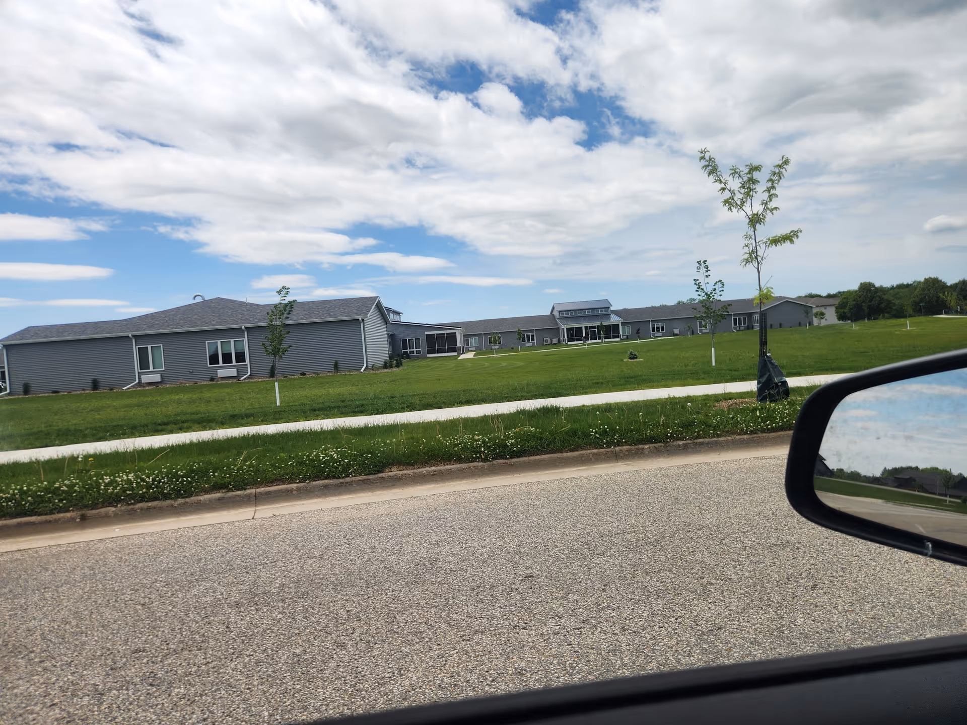 Wide exterior view of a gray senior living campus with a green lawn and road.