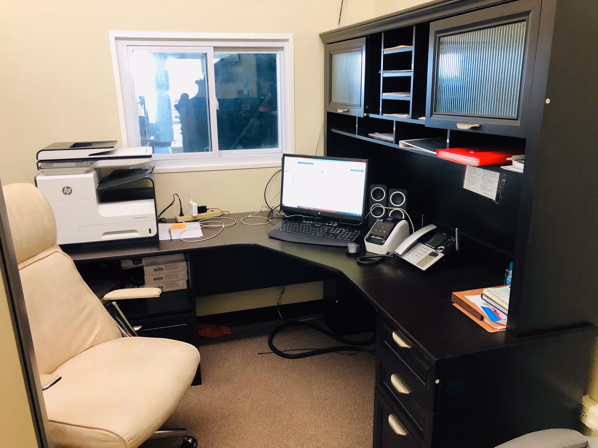L-shaped dark wood desk with computer, printer, and office gear in a facility office.