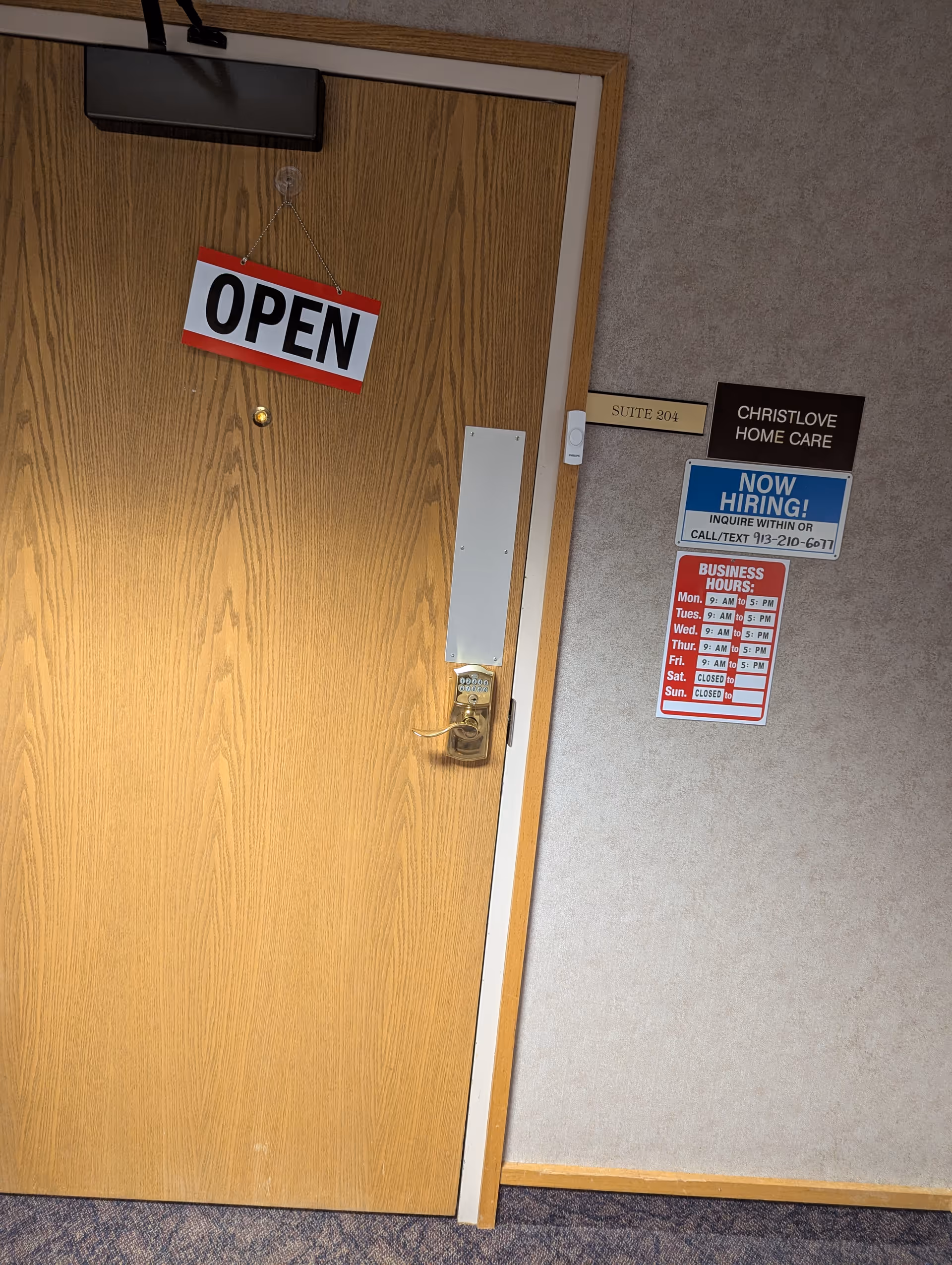 A wooden door displays an OPEN sign beside office suite plaques on a beige wall.