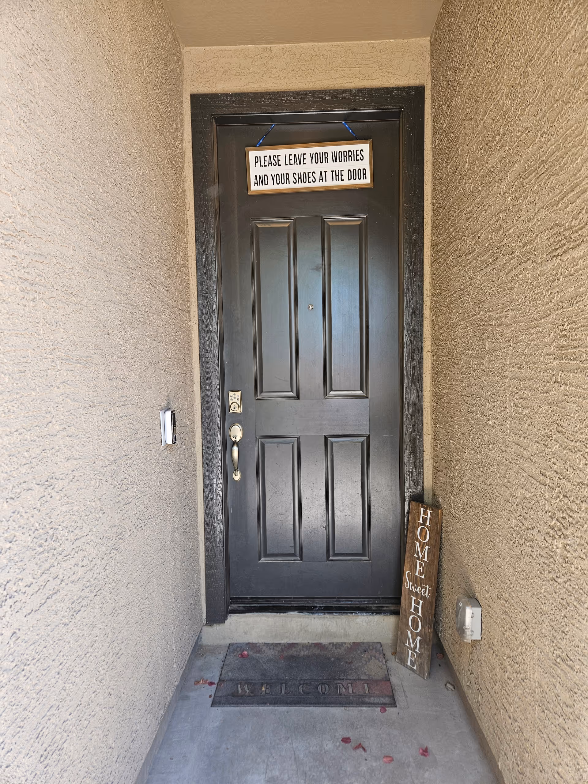 Narrow entry doorway with signs, a welcome mat, and a 'Home Sweet Home' plaque.