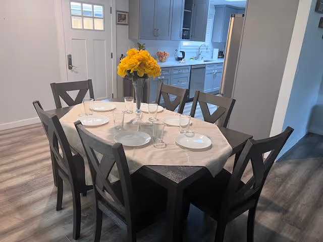 Dining table set for a meal with a yellow flower centerpiece in a kitchen-dining area.
