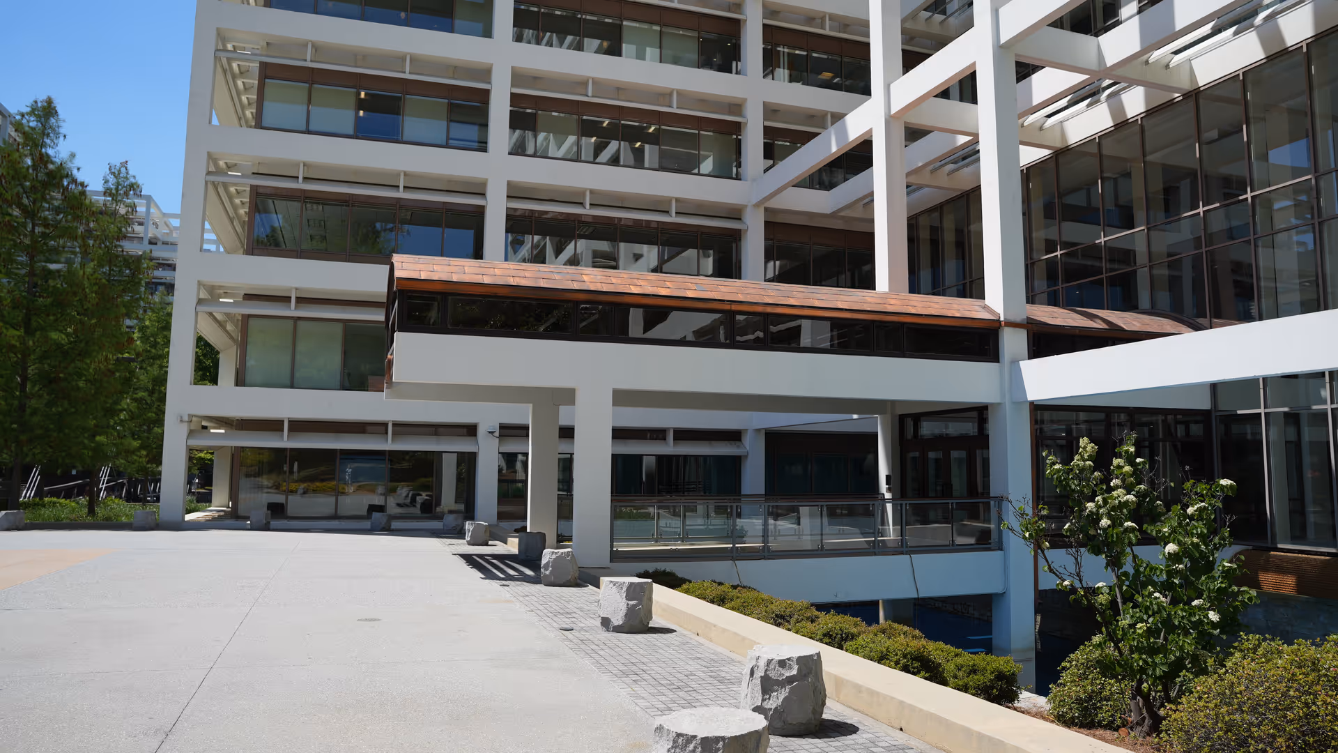 Modern multi-story building exterior with glass walls and an outdoor plaza.