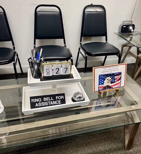 Lobby seating area with glass coffee table, flip calendar, bell, and assistance sign.