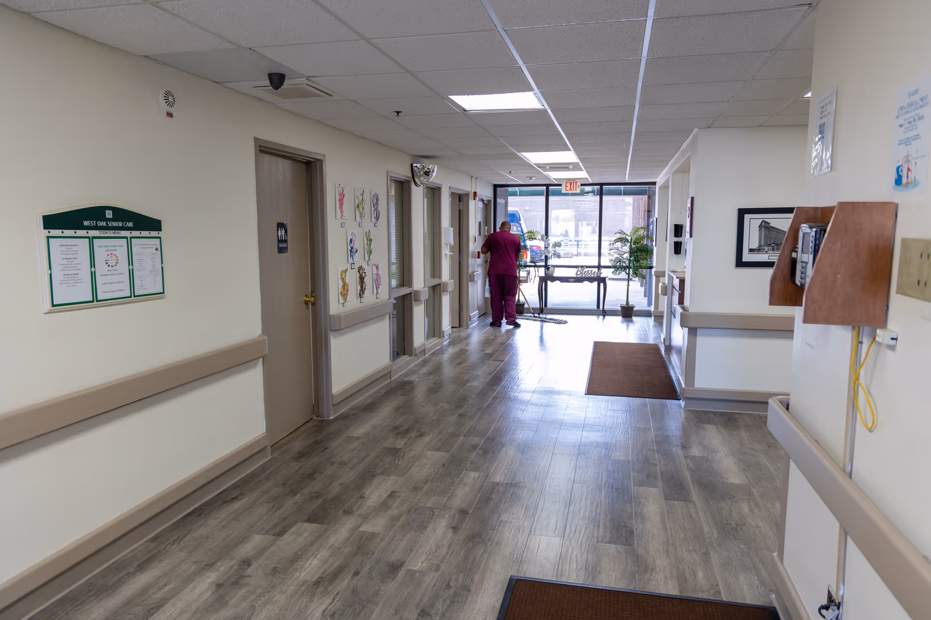 Interior hallway of West Oaks Senior Care & Rehab Center with doors, bulletin boards, and nurse.