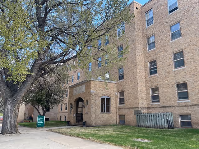 Exterior view of a brick building with an arched entrance and trees nearby.