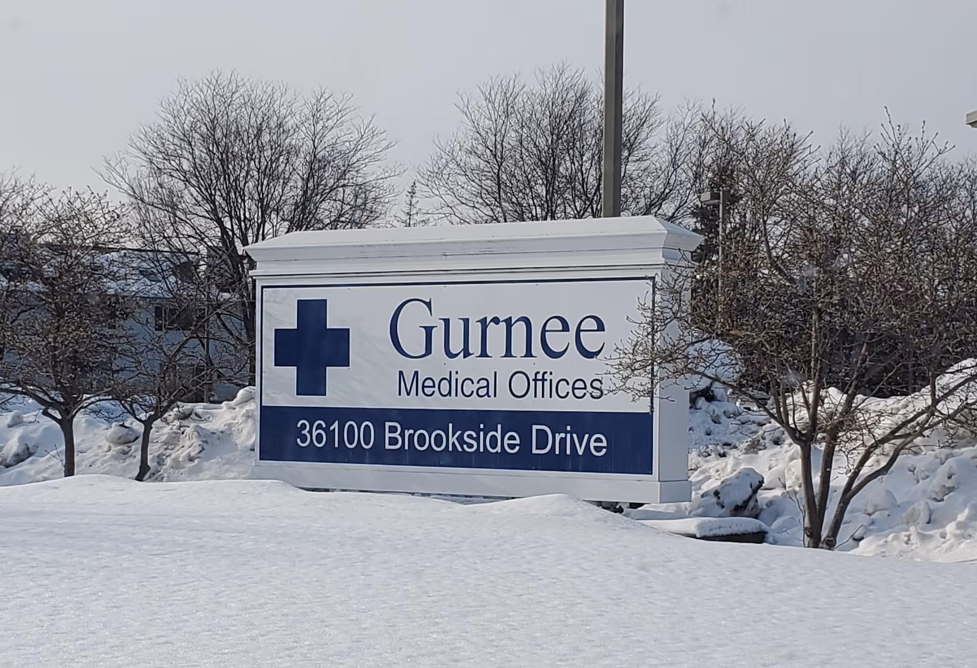 Outdoor sign reading Gurnee Medical Offices on snowy grounds with leafless trees