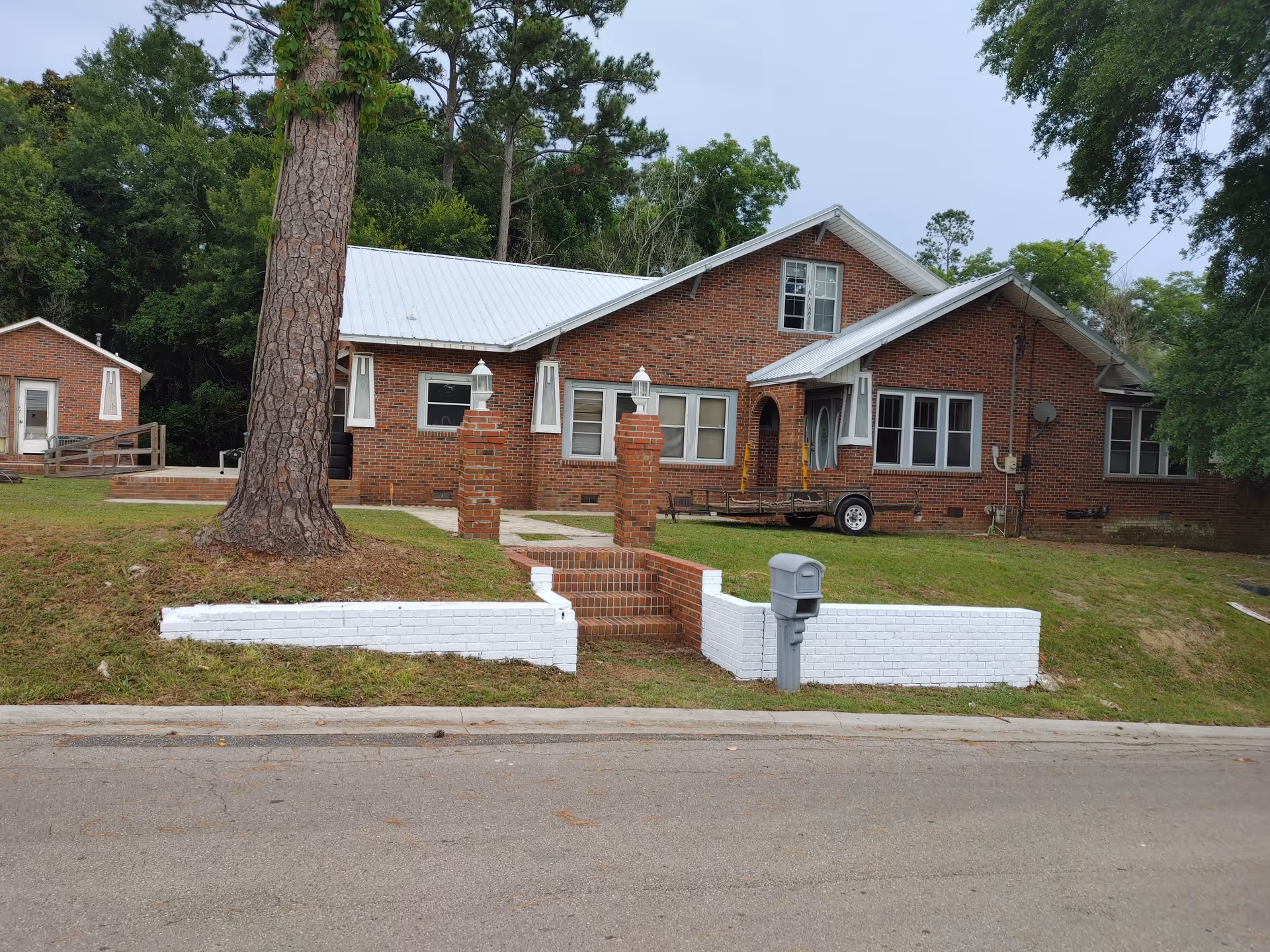 Brick senior living facility with a white front porch, steps, mailbox, and trees nearby.