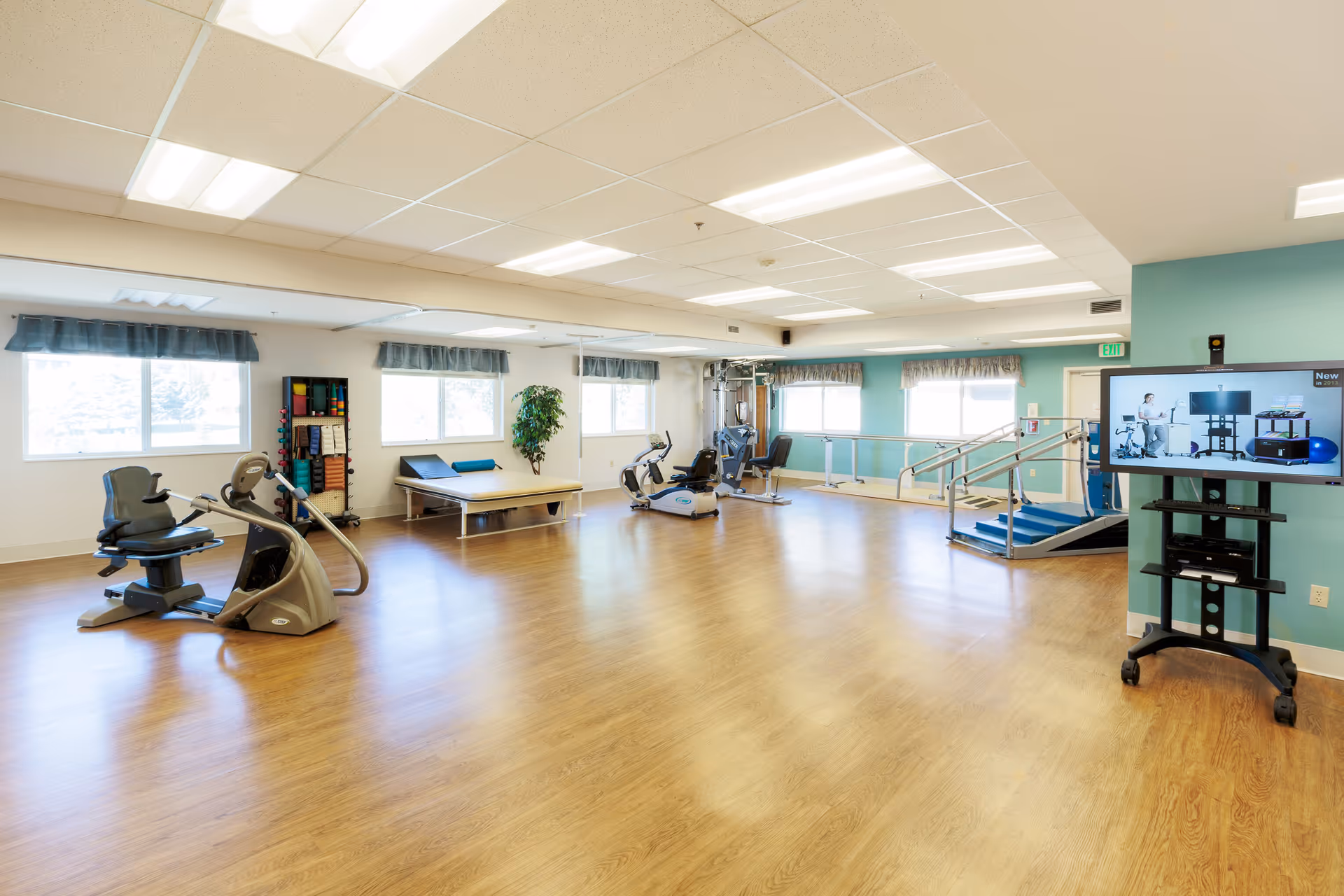 Spacious interior gym in a post-acute facility with exercise equipment and a TV.